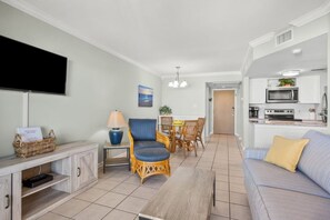 Ein modernes Wohnzimmer mit Flachbildfernseher, eine Essecke mit Korbstühlen und eine Küche mit weißen Schränken.
