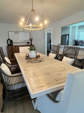 A dining area with a large wooden table, wicker chairs, and a hanging light fixture. - Spacious 3BR home with private pool and water views in Yulee. Easy access to Amelia Island. (Yulee)