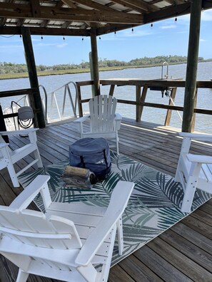 Una terrazza coperta con poltrone Adirondack bianche, un tappeto decorato e una borsa blu sul pavimento.