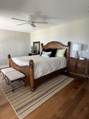 A bedroom with a wooden bed, a nightstand, a lamp, a mirror, and a ceiling fan. - Spacious 3BR home with private pool and water views in Yulee. Easy access to Amelia Island. (Yulee)