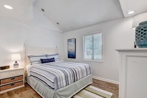 Une chambre à coucher avec un lit, une table de chevet, une lampe, un tableau, une fenêtre et un objet décoratif sur le mur.