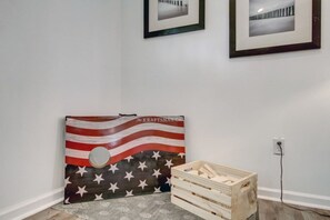 A room with a wooden crate, a framed artwork with a circular cutout, and a wall-mounted outlet. - Amelia Island Home with Fire Pit and Outdoor Shower, 1 Mile to the Beach (Fernandina Beach)