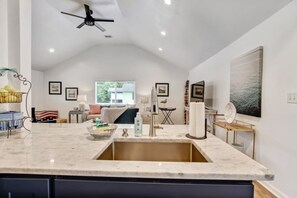 Une cuisine dotée d’un grand îlot central, d’un ventilateur de plafond et donnant sur l’espace de vie.