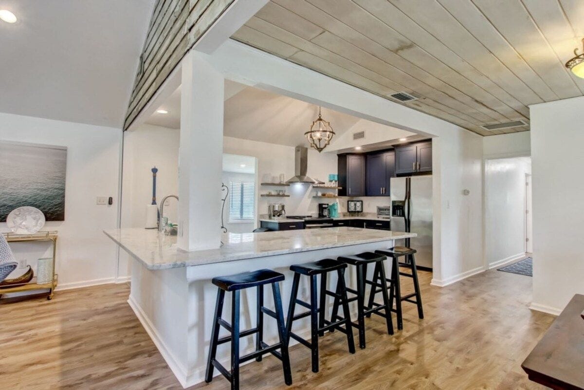 A modern kitchen with a central island, bar stools, and a view into the dining area.
