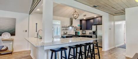Una cocina moderna con una isla central, taburetes de bar y vistas al área de comedor.