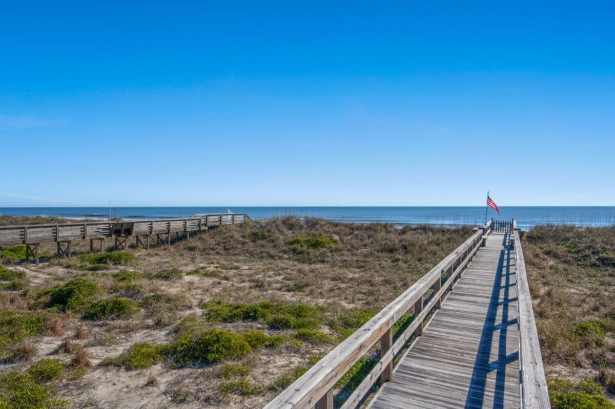 Une promenade en bois menant à une plage, avec un drapeau au bout.