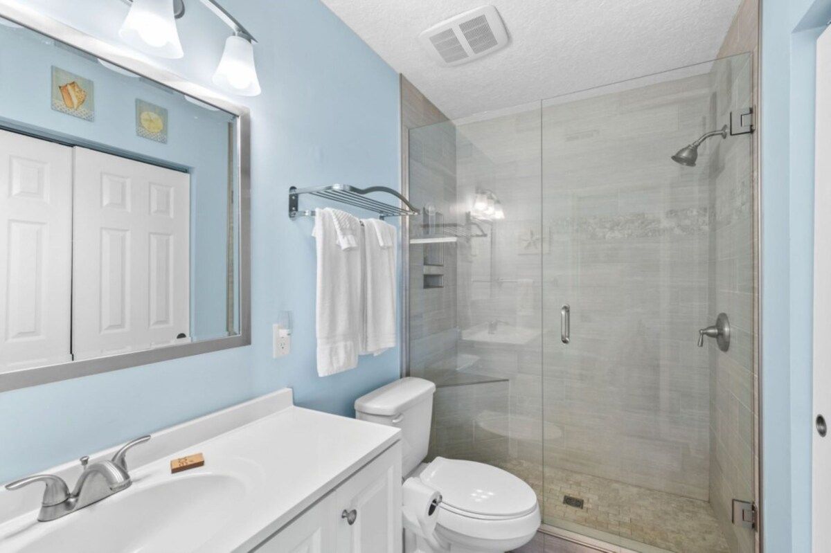 Une salle de bain avec un lavabo blanc, des toilettes, une douche en verre et un porte-serviettes.