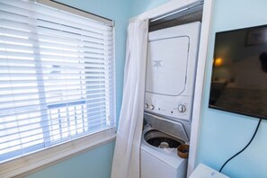 Una sala amb bugaderia, amb rentadora i assecadora, una finestra amb persianes, i un televisor fixat a la paret.