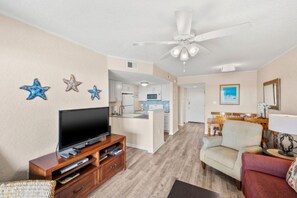 Ein Wohnzimmer mit Fernseher, Deckenventilator und einer Küche im Hintergrund.