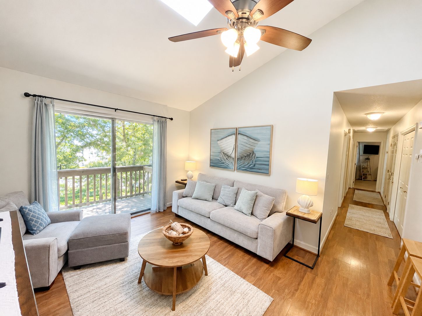 A spacious living room with a ceiling fan, a sofa set, a coffee table, and a view of the outdoors through a sliding glass door.