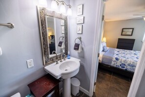 A bathroom with a sink, mirror, and towel rack. There is a bed with a patterned bedspread in the adjacent room. - Oceanfront Amelia Island Condo with Ocean View Balcony, Elevator, and Pool (Fernandina Beach)
