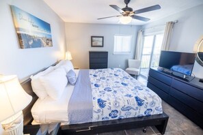 Une chambre à coucher comprenant un lit, un ventilateur de plafond, une télévision, une commode et une fenêtre avec des stores.