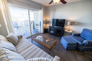 Un salon comprenant un canapé, un pouf, une télévision et une table basse en verre.