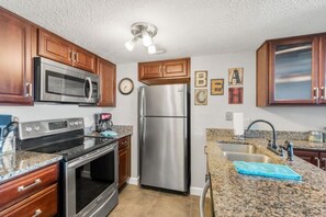 A kitchen with stainless steel appliances, wooden cabinets, granite countertops, and a clock on the wall. - Oceanfront Amelia Island Condo with Ocean View Balcony, Elevator, and Pool (Fernandina Beach)