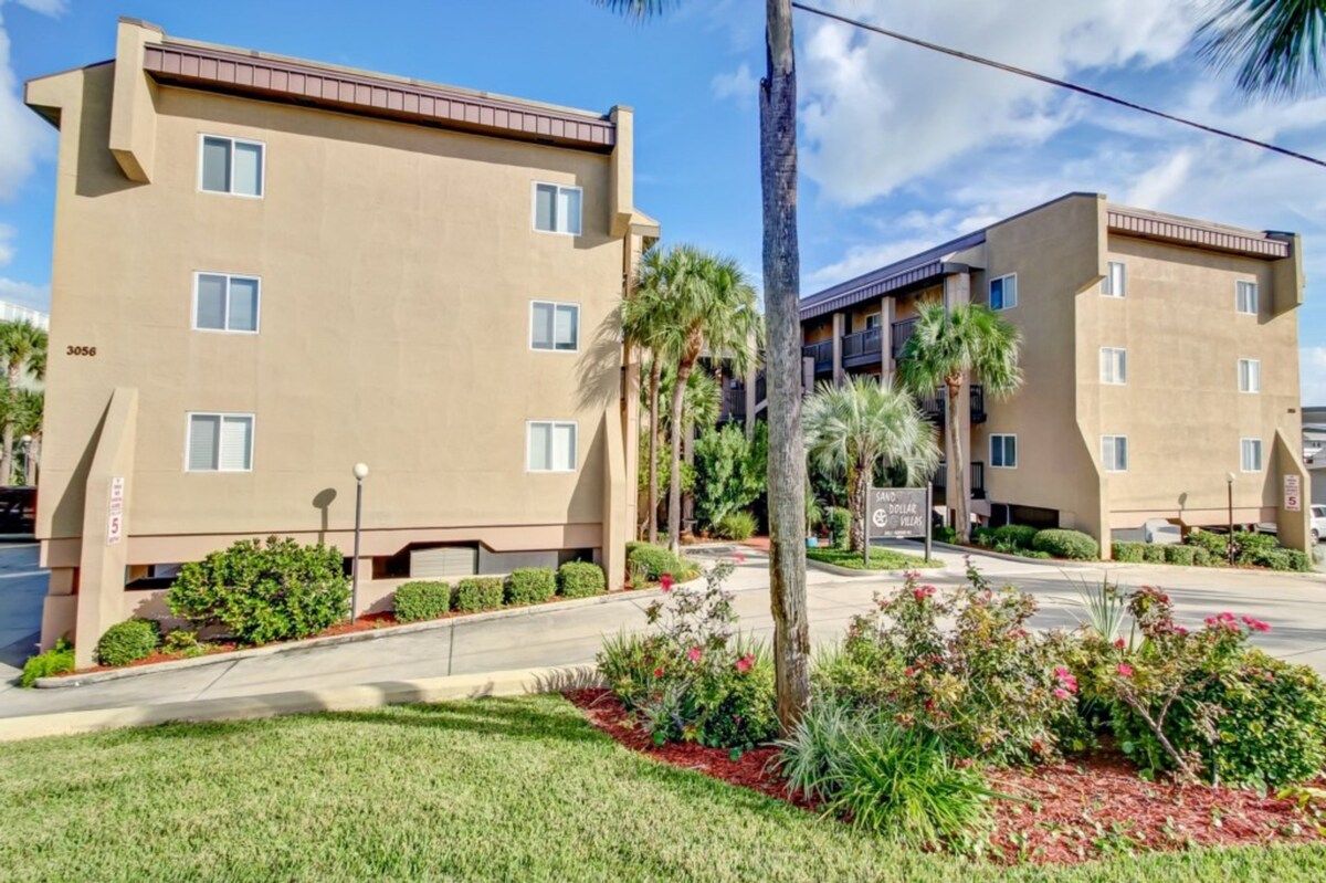 A multi-story residential building with a beige exterior, numbered 3056, featuring a landscaped front yard with palm trees and shrubs.