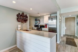 A modern kitchen with a central island, built-in appliances, and a decorative wall piece. - Waterfront Amelia Island Condo with Ocean View, Elevator Access, and Pool (Fernandina Beach)