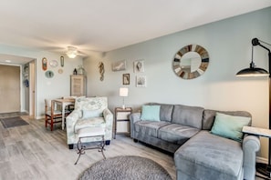 A living room with a grey sofa, a floral armchair, a small table, and a lamp. - Waterfront Amelia Island Condo with Ocean View, Elevator Access, and Pool (Fernandina Beach)