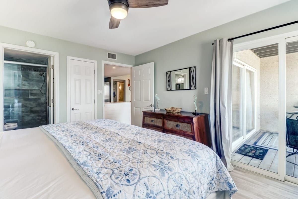 Une chambre à coucher comprenant un lit, une commode, un miroir et une porte-fenêtre coulissante donnant sur un balcon.