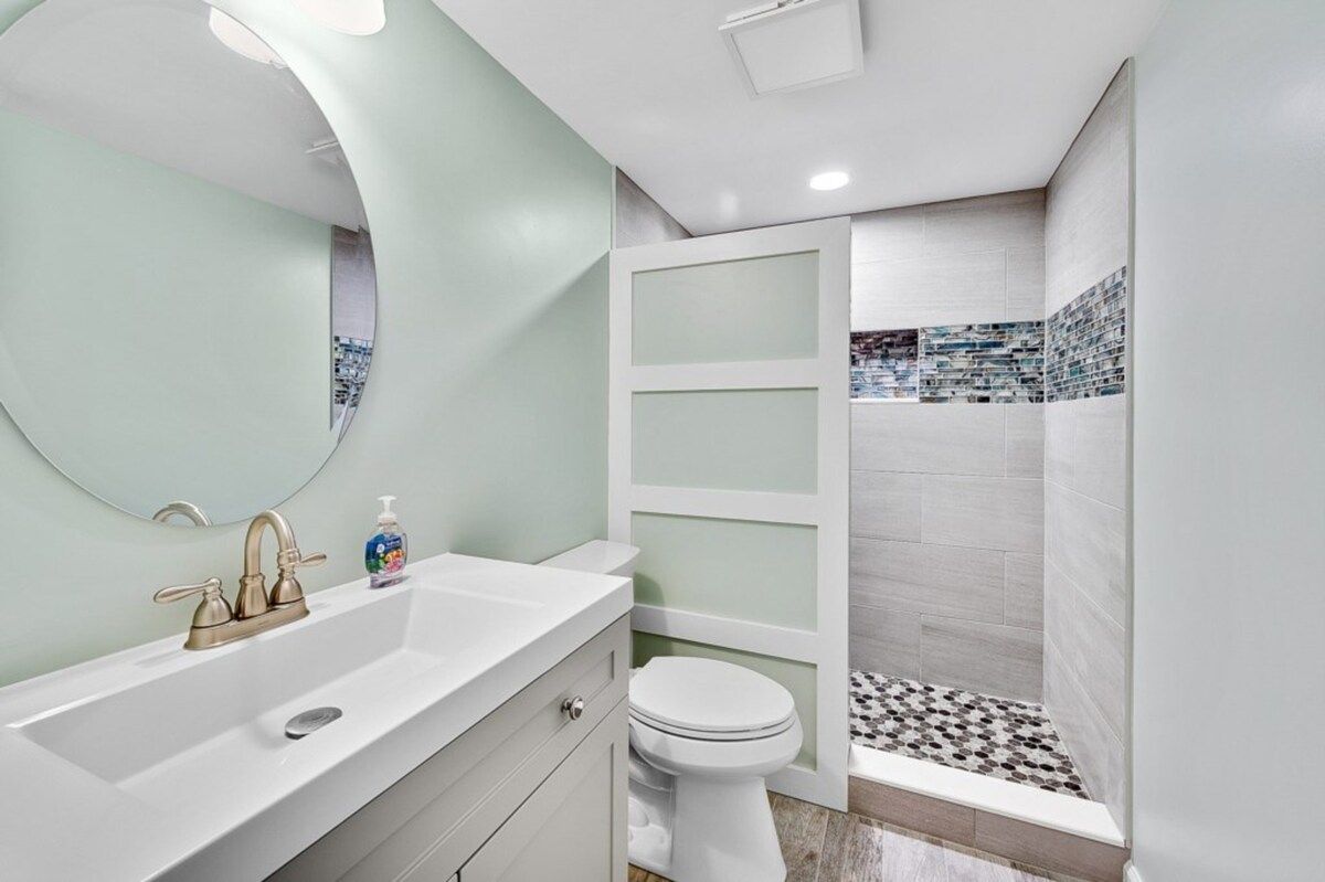 A bathroom with a white sink, a mirror, a toilet, and a shower area with patterned tiles.