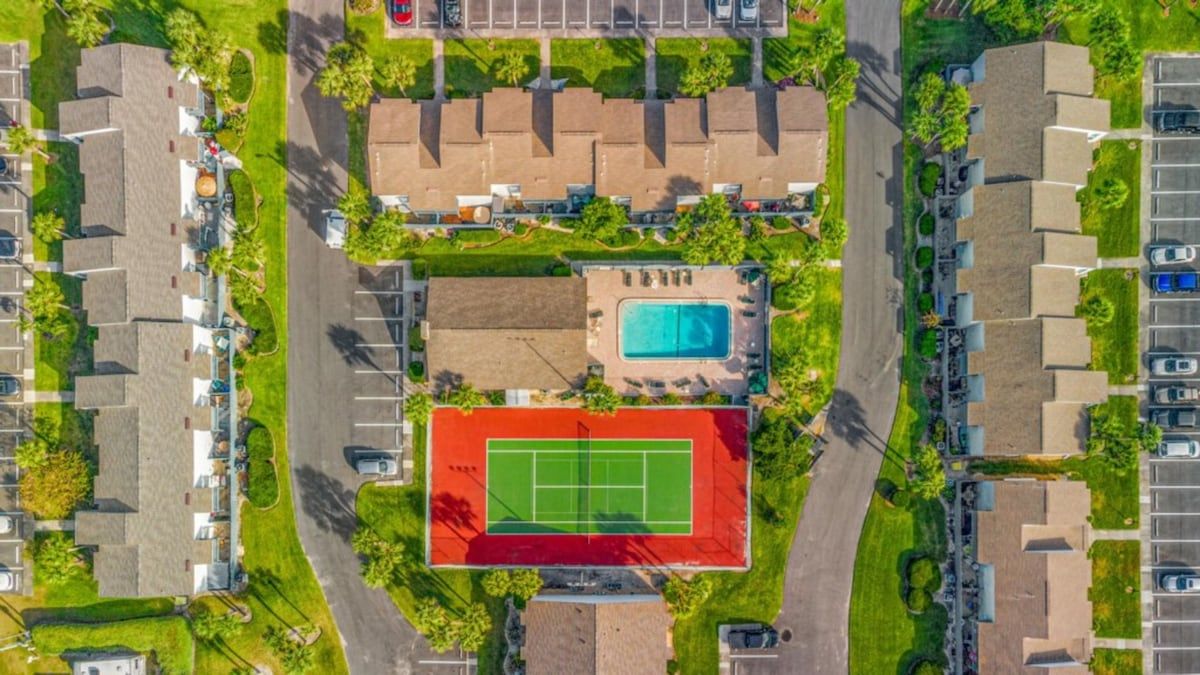 An aerial view of a residential area with a tennis court, swimming pool, and multiple parking lots.