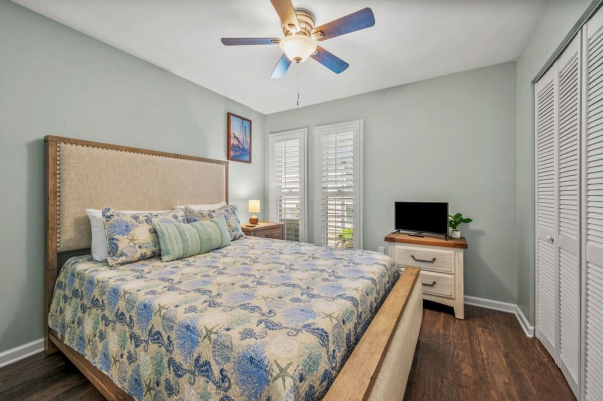 A bedroom with a bed, a nightstand, a TV, a ceiling fan, and a closet.