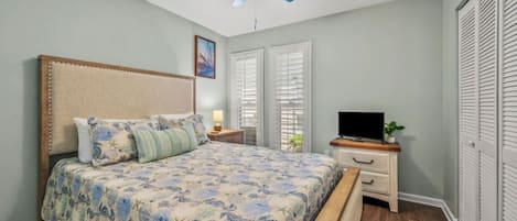 A bedroom with a bed, a nightstand, a TV, a ceiling fan, and a closet.