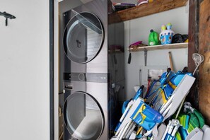 A laundry room with two washing machines and a shelf with cleaning supplies. - 3BR Condo • Pool • Walk to Beach • Sleeps 6 (Fernandina Beach)