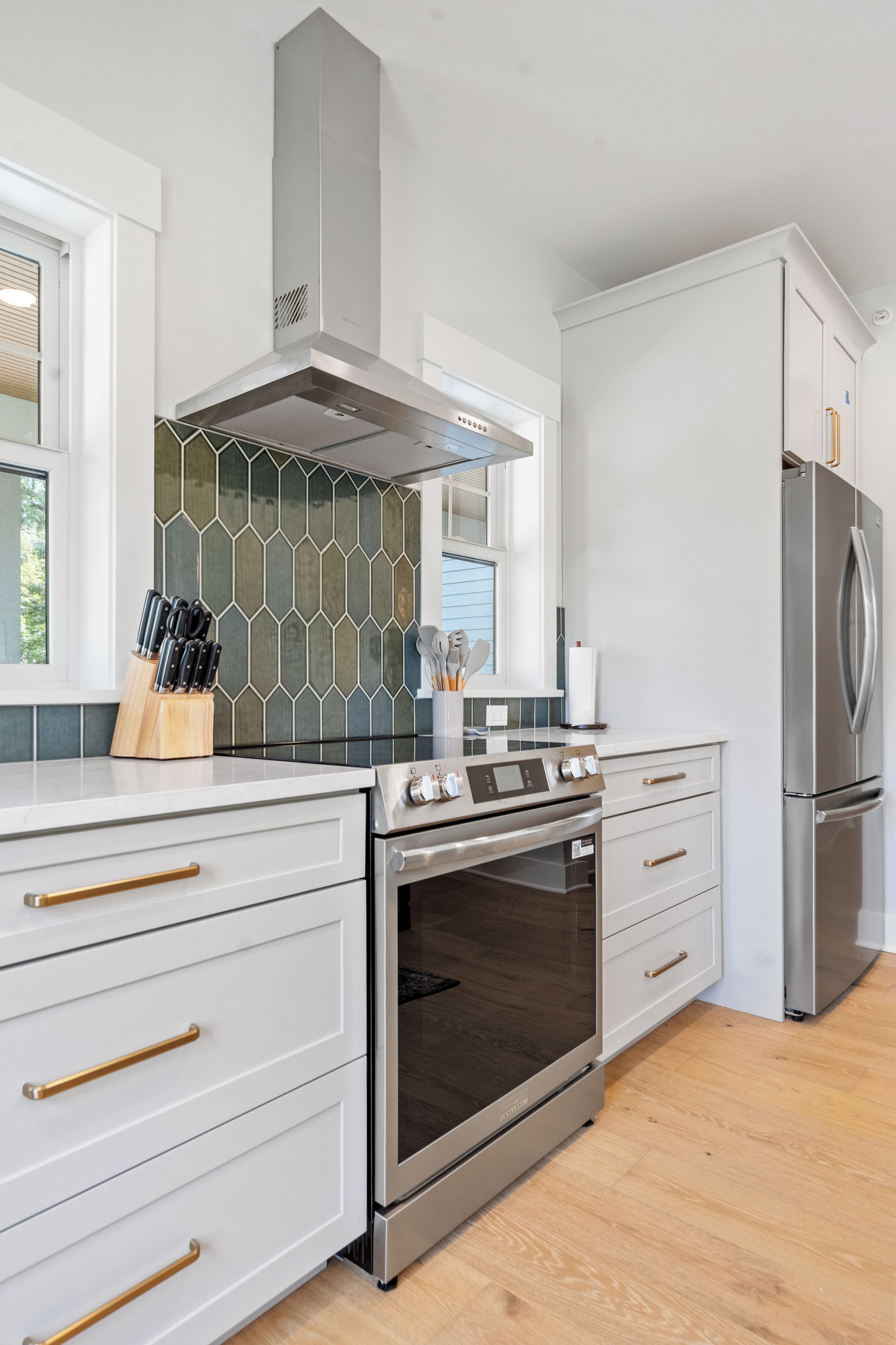 A modern kitchen with a stainless steel range, oven, and refrigerator, white cabinetry, and a hexagonal tile backsplash.