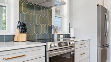 A modern kitchen with a stainless steel range, oven, and refrigerator, white cabinetry, and a hexagonal tile backsplash.
