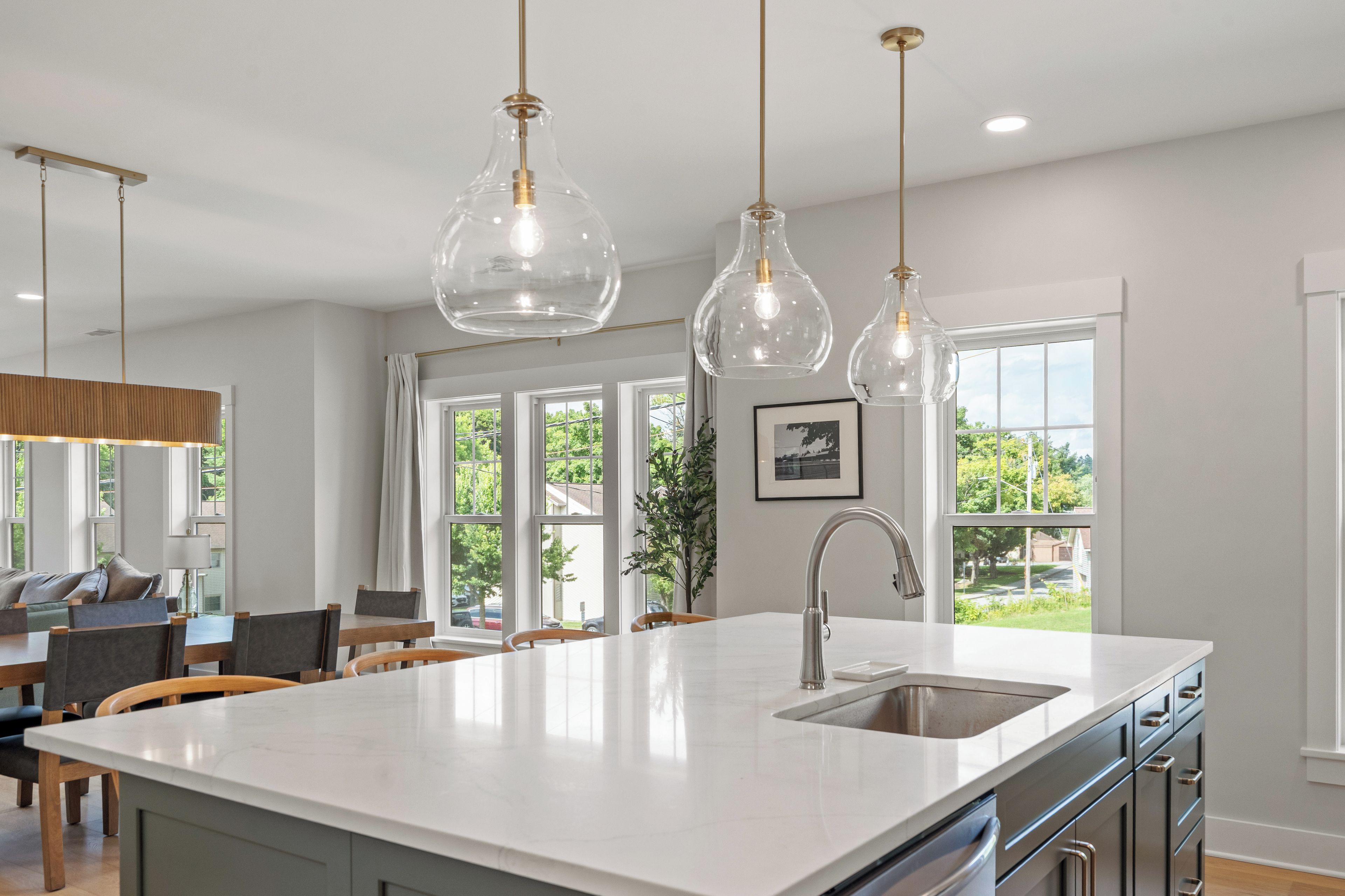A modern kitchen with a large island, pendant lights, and a view of the outdoors through large windows.