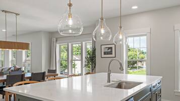 A modern kitchen with a large island, pendant lights, and a view of the outdoors through large windows.