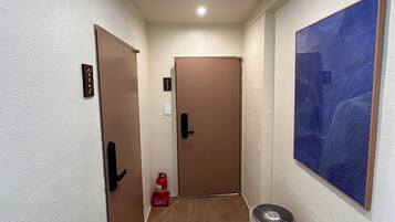 A narrow hallway with wooden flooring, two doors, a fire extinguisher, and a standing heater.