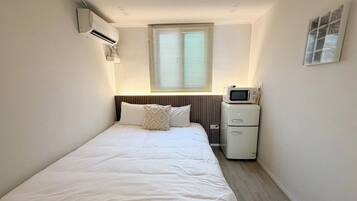 Habitación de hotel con cama, una mesita de noche con microondas y una ventana con persianas.