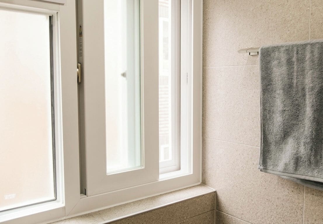 Un baño con ventana, toallero y pared con azulejos.