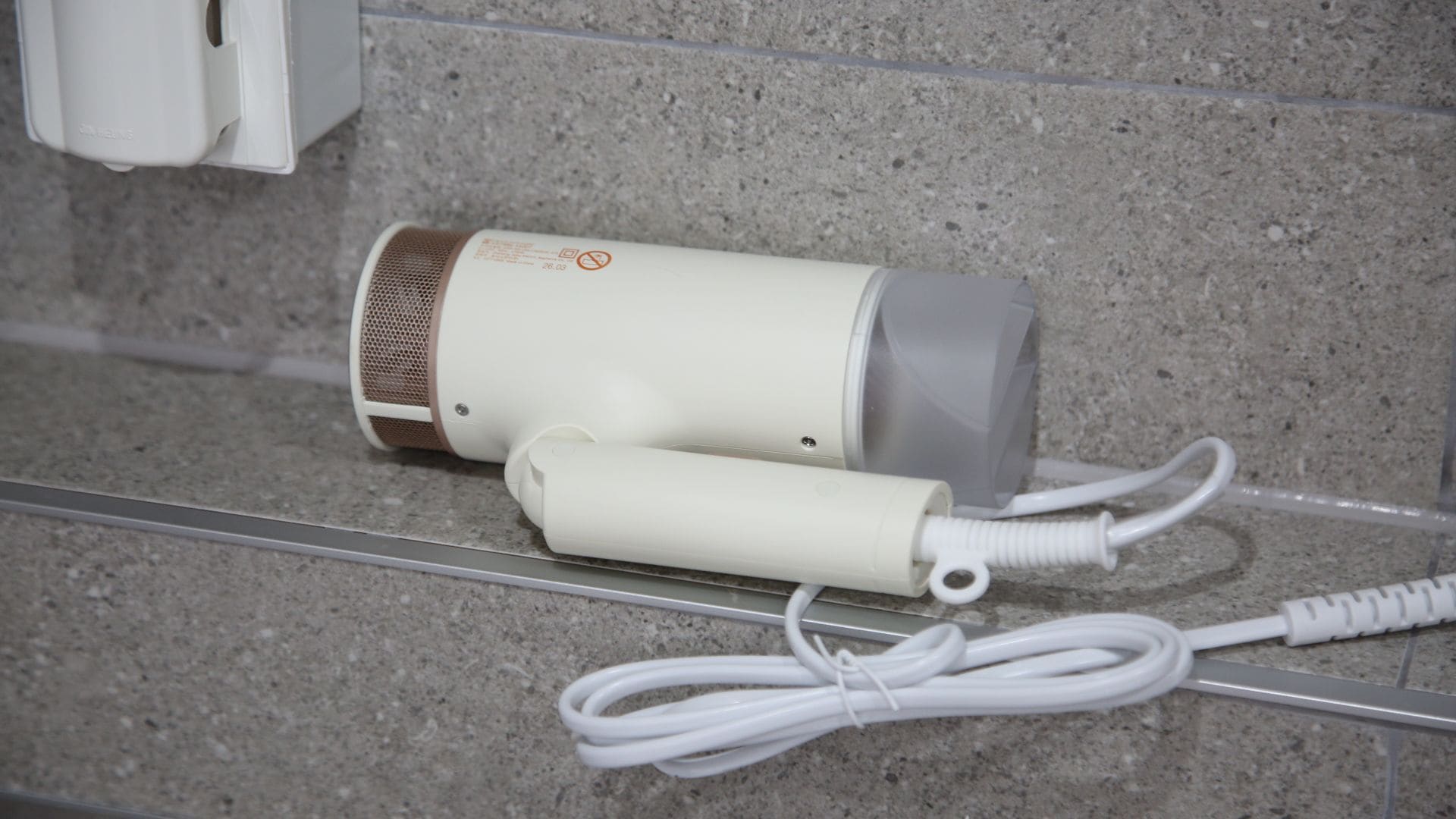 Un secador de pelo y su cable de alimentación sobre un suelo de baldosas.