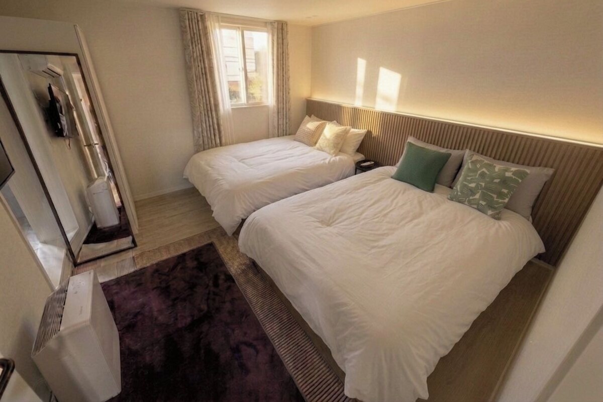 Quarto de hotel com duas camas, janela, radiador e espelho.