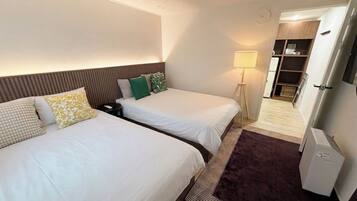 A hotel room with two beds, a bedside table, a lamp, a wardrobe, and a refrigerator.