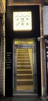 Entrada de un edificio con un letrero iluminado sobre la puerta y una escalera que da acceso al interior.