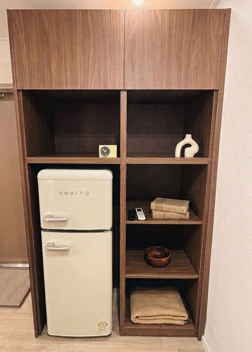A wooden cabinet with a white appliance, shelves with books, a bowl, and a folded towel.