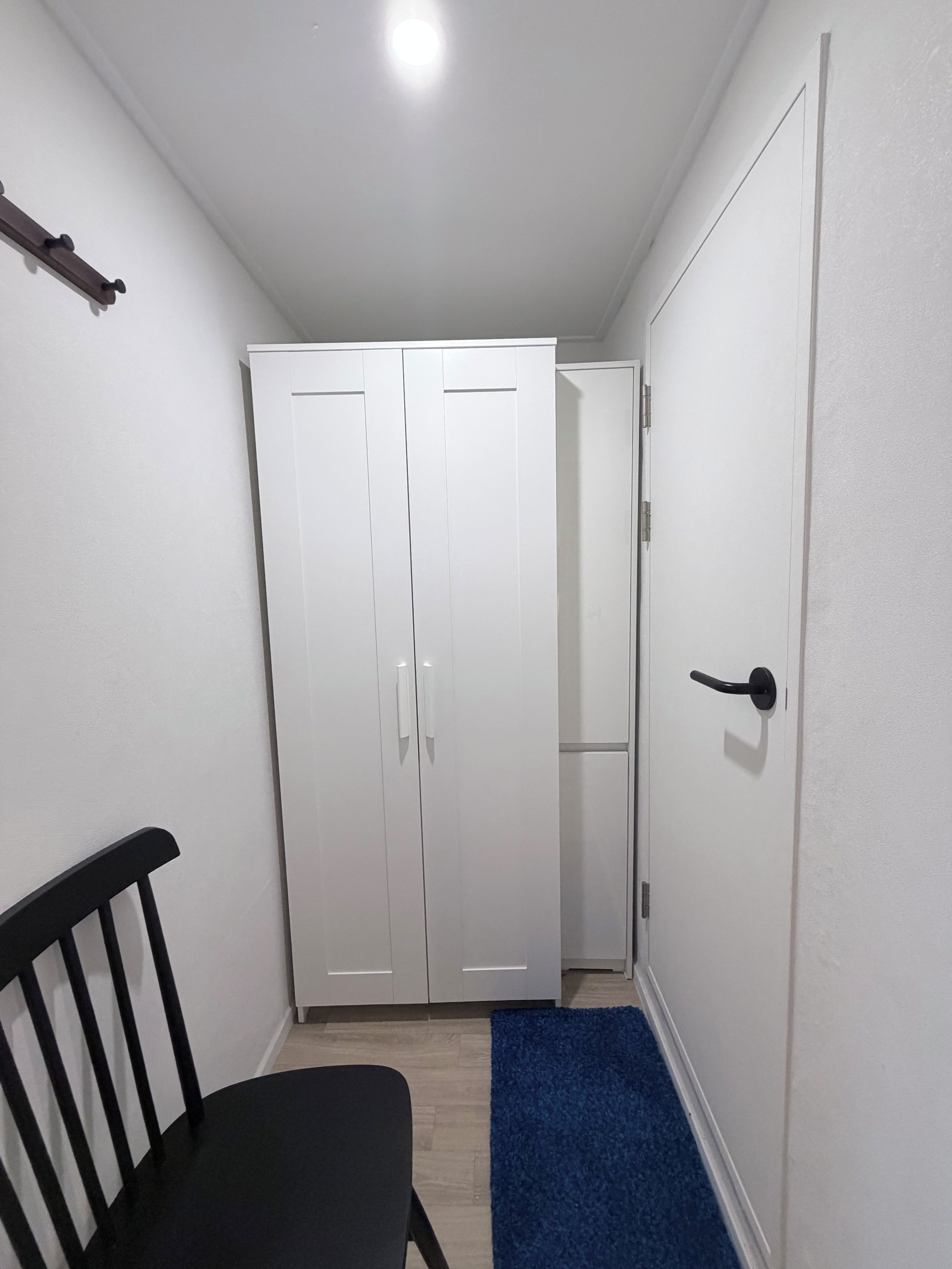A narrow hallway with a black chair, a blue rug, and white double doors.