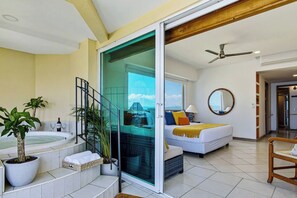 A hotel room with a balcony, a bathtub, a bed with a view, and a ceiling fan. - Beachfront-2 BR Plus 2 BR-Apartment Shared Balcony (Puerto Vallarta)