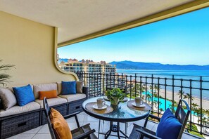 A balcony with a sofa, chairs, and a table with cups and a plant. - Beachfront-2 BR Plus 2 BR-Apartment Shared Balcony (Puerto Vallarta)