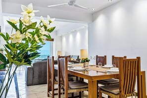 A dining area with a wooden table and chairs, a sofa, and a view of the sea. - Beachfront-2 BR Plus 2 BR-Apartment Shared Balcony (Puerto Vallarta)