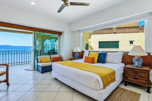 A hotel room with a large bed, a balcony with a view, and a ceiling fan. - Beachfront-2 BR Plus 2 BR-Apartment Shared Balcony (Puerto Vallarta)