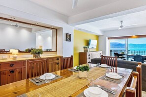 A dining area with a wooden table set for four, a sofa, and a view of the sea. - Beachfront-2 BR Plus 2 BR-Apartment Shared Balcony (Puerto Vallarta)
