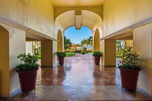 A corridor with a clear view of a landscaped area and palm trees, leading to a building entrance. - Beachfront-2 BR Plus 2 BR-Apartment Shared Balcony (Puerto Vallarta)