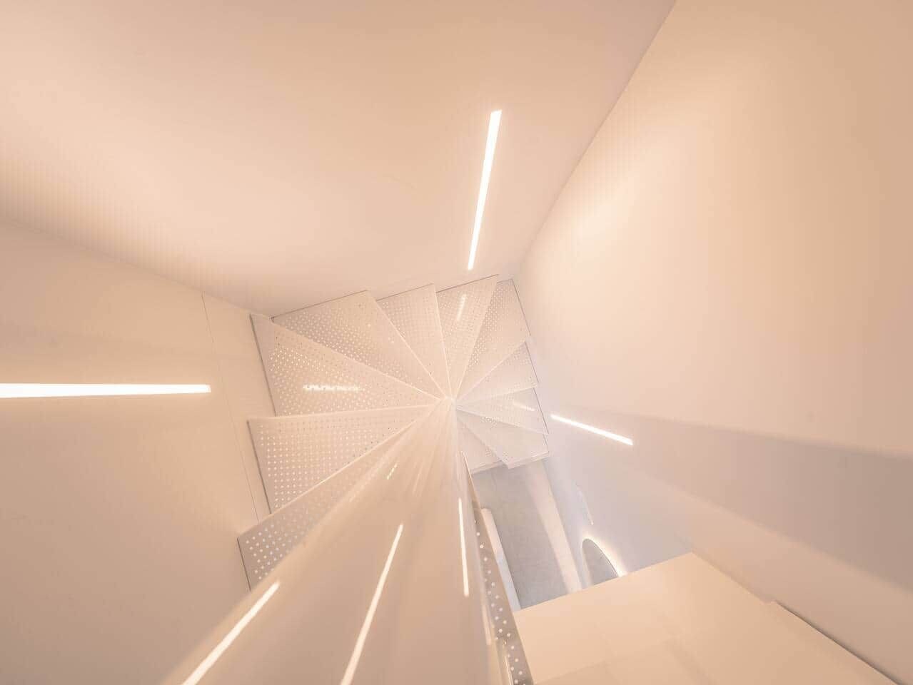 A modern interior with a geometric staircase design, featuring a central light source and a patterned wall.