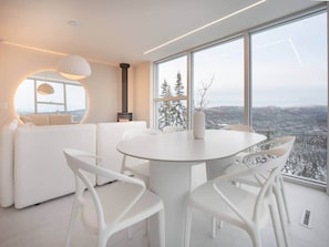 A modern interior with a round dining table, white chairs, and a sofa. - BLACK MIRROR / Glass Retreat Above the Mountains (Capitale-Nationale)