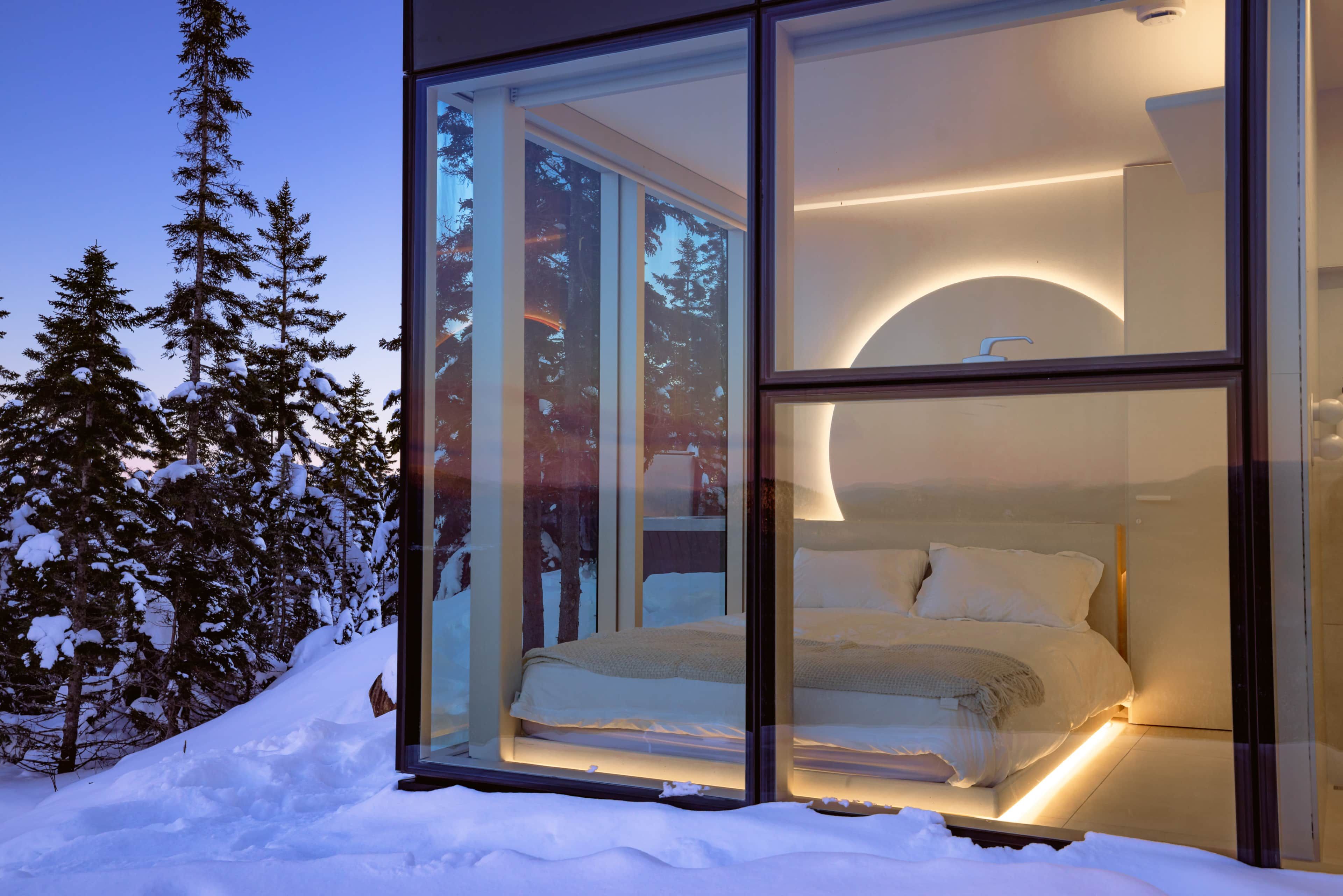 A modern bedroom with a bed, a nightstand, and a large window overlooking a snowy landscape.