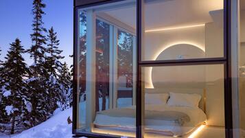 A modern bedroom with a bed, a nightstand, and a large window overlooking a snowy landscape.
